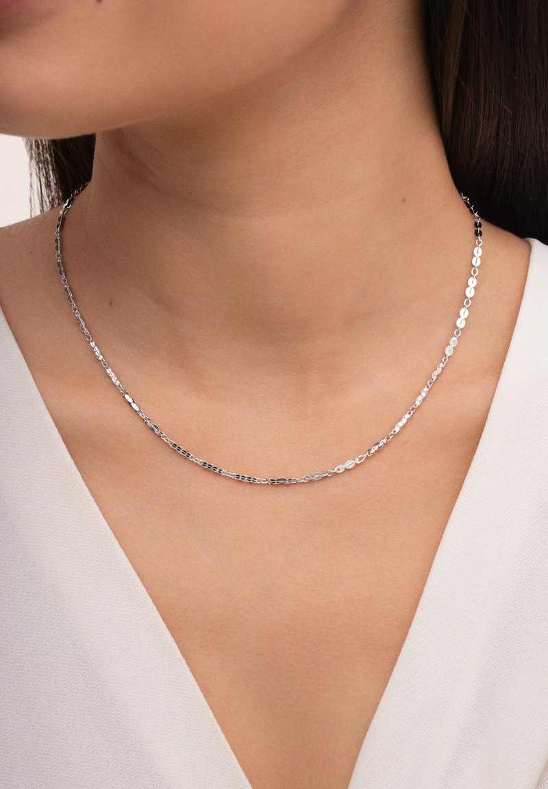 Collana in argento con un design delicato a maglie ovali piatte. La catena è liscia, con una finitura lucida, che riposa elegantemente sulla pelle.
