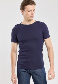 T-shirt attillato a maniche corte di colore blu navy, realizzato in tessuto rigato, con colletto tondo e spalle senza cuciture, abbinato a jeans in denim scuro.