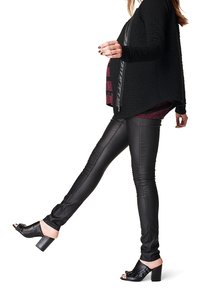 Cárdigan negro texturizado con un diseño asimétrico, combinado con pantalones de cuero negro ajustados y sandalias negras de tacón.