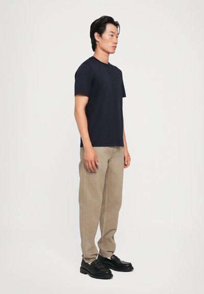T-shirt bleu marine à manches courtes associé à un pantalon beige à jambes larges et des chaussures noires. Le tissu semble lisse avec des détails de couture subtils.