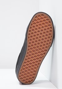 Svart sneakersula med en texturerad gummibotten som visar ett diamantmönster, i kontrast till en brun gummibas.