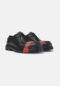 Zapatillas de cuero negro con una puntera de goma roja en contraste, con un diseño clásico de cordones y suela de goma texturizada.
