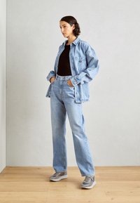 Chaqueta de mezclilla azul clara y jeans, top negro ajustado, zapatillas grises, corte relajado, bolsillos visibles, detalles de botones y textura suave.