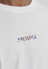 Camiseta de algodón blanca con un estampado gráfico en el pecho en texto azul y naranja, con cuello redondo y mangas cortas.
