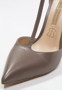 Talons aiguilles en cuir gris foncé avec un bout pointu et un côté ouvert. Présente une fine bande et une texture lisse et polie.
