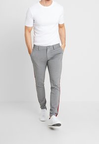 Szare spodnie o dopasowanym kroju z gładką fakturą, z czerwonymi bocznymi paskami. Połączone z dopasowanym białym T-shirtem i białymi trampkami.