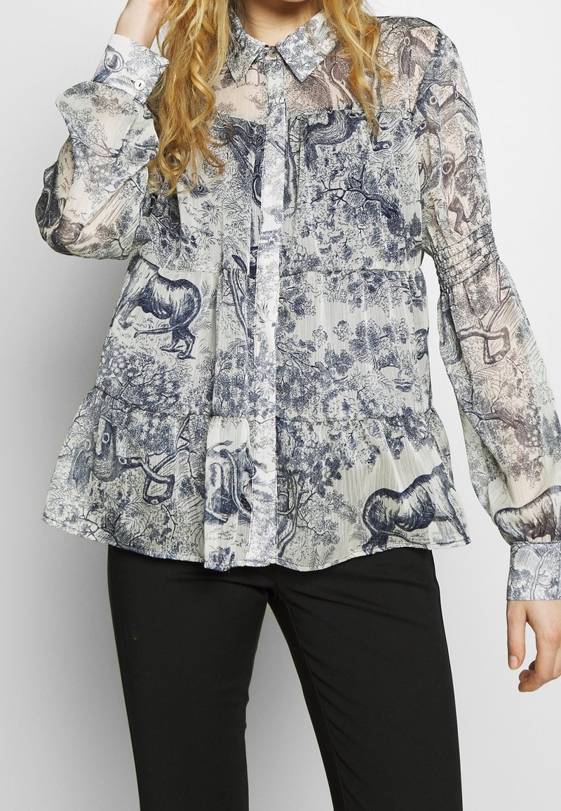 Transparent skjorta med långa ärmar och knäppning, som har ett mönster i blått och vitt med djur och natur, med en volangnert kjol och krage.