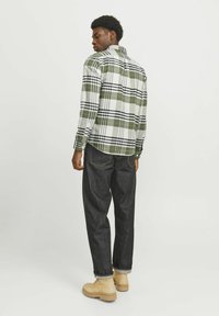 Camisa de franela a cuadros en verde y blanco con acentos en negro, con puños abotonados, combinada con pantalones de mezclilla oscuros y botas beige.