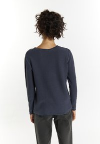 Tricou cu mânecă lungă de culoare bleumarin, cu un model texturat de tip waffle, guler rotund și croială lejeră, asociat cu pantaloni gri.