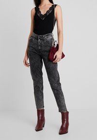 Svart ribbad bodysuit med spetsdetaljer, hög midja, blekta grå jeans och burgundy texturerade ankelstövlar. Liten burgundy kuvertväska.