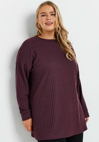 Lila rättrandig långärmad topp med rundad halsringning, med neddragna axlar och sidoflikar för ökad rörelsefrihet. Mjuk textur.