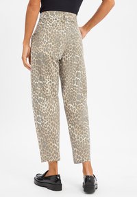 Beige en grijs leopardprint hoge taille broeken met een relaxte pasvorm, zijzakken en een gladde textuur. Zwarte schoenen afgebeeld.