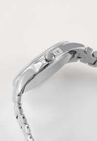 Montre en argent avec un boîtier en métal poli, une lunette texturée et un bracelet à maillons, dotée d'une couronne ronde sur le côté.
