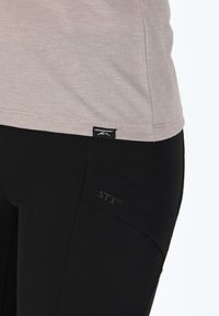 Top grigio chiaro con strisce testurizzate e un'etichetta nera, abbinato a pantaloni neri aderenti con logo STX e cuciture che snelliscono.