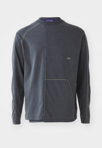 T-shirt à manches longues de couleur gris foncé en coton, avec des coutures jaunes contrastantes, un col ras du cou et un logo sur le devant.