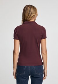 Bordowy polo z klasycznym kołnierzykiem, krótkimi rękawami i gładką fakturą. Noszony z dżinsami, widok z tyłu.