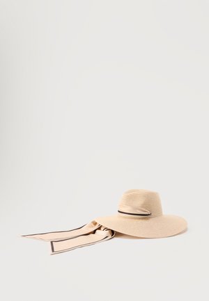 Chapeau de soleil beige à large bord avec un long ruban beige bordé de noir noué autour de la base, posé sur une surface gris clair.