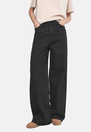 Vaqueros negros de pierna ancha hechos de mezclilla, con una cintura alta, dos bolsillos frontales y un diseño limpio y minimalista. Se combinan con una blusa de color beige claro.