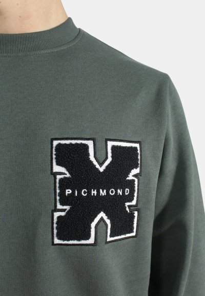 Felpa verde con una toppa nera testurizzata con un contorno bianco e il testo "PICHMOND" al centro. Collo alto e materiale a coste.