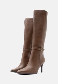 Καφέ δερμάτινες μπότες μέχρι το γόνατο με μυτερές μύτες, στιλέτο τακούνια και χρυσές αγκράφες στις λωρίδες λίγο πάνω από τον αστράγαλο. Λείος υφασμάτινος τύπος.