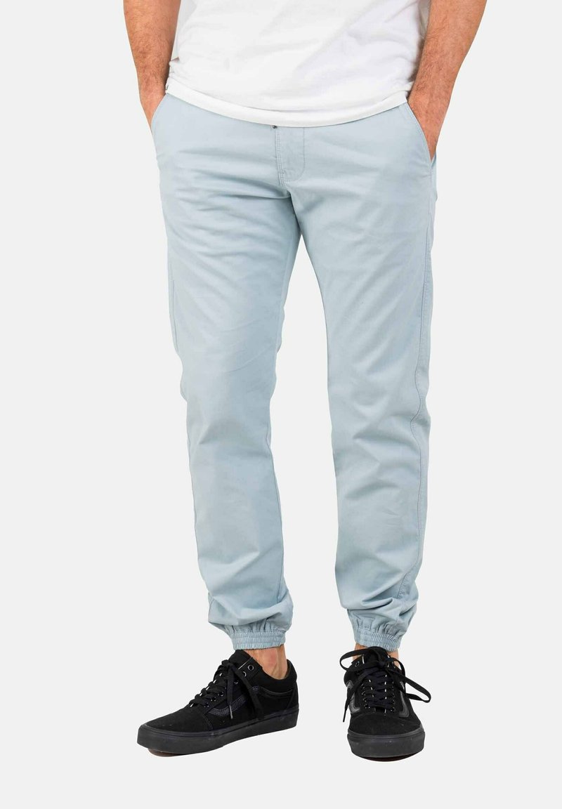 Chinos azul claro con un corte ajustado, puños elásticos y bolsillos laterales; combinados con zapatillas negras para un look casual.