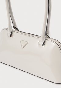 Γυαλιστερή τσάντα ώμου εκρού με δύο χερούλια, κλείσιμο με φερμουάρ και τριγωνικό ασημένιο λογότυπο. Διαθέτει μαύρο περιθώριο κατά μήκος των άκρων για αντίθεση.