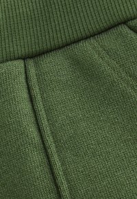 Der grüne gestrickte Stoff weist eine strukturierte Oberfläche mit geripptem Bund und Nähten auf, die ein glattes Finish und ein einheitliches Muster zeigt.