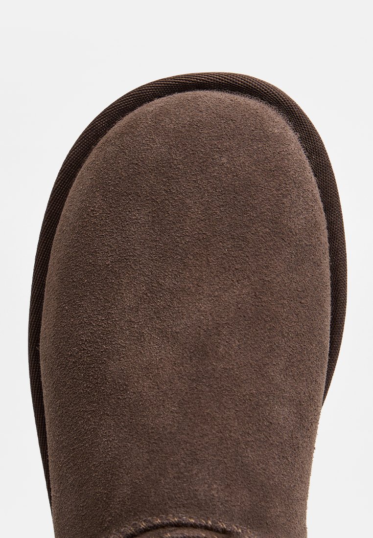 Botte en suede marron avec un bout arrondi. Présente une texture lisse et une bordure en tissu marron foncé contrastant le long du bord supérieur.