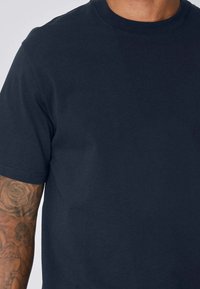 T-shirt en coton bleu marine à col rond et manches courtes. Texture lisse sans motifs visibles. Gros plan sur le tissu.