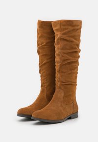 Bottes hautes en daim marron avec un design légèrement froncé, bouts arrondis et un petit talon carré. Texture douce et détails minimalistes.