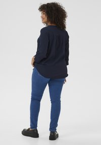 Marineblaue Bluse mit langen Ärmeln und lockerer Passform, kombiniert mit blauen Skinny-Jeans und schwarzen Plateauschuhen. Glatter Stoff mit subtiler Textur.