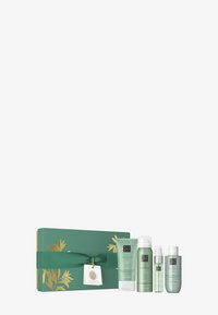 Cadeau en boîte verte et dorée avec un ruban, contenant quatre produits de soin Ritual of Jing en vert : un masque pour les mains, un gel douche, une brume et une huile corporelle.