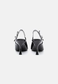 Tacones slingback de charol negro con punta afilada, tacón alto de aguja y correa ajustable que presenta acentos de textil con marca.