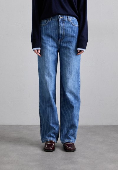 Lys blå denim jeans med lodrette hvide striber, højtaljet og bred benpasform. Båret med en mørk trøje og burgunder sko.