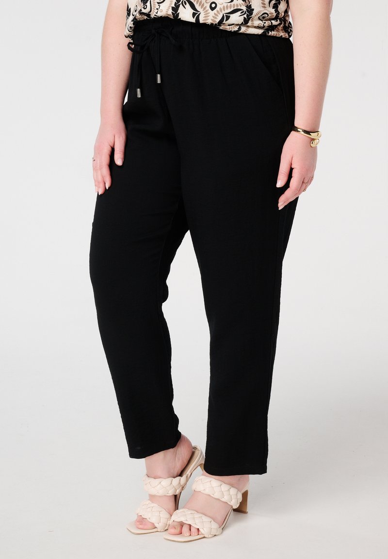 Zwarte elastische taillebroek met een losse pasvorm en zijzakken, gecombineerd met beige gevlochten hakken. Vlakke, gladde textuur.