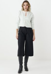 Jasnoszary kardigan z dzianiny z falbanką, z zapięciem na guziki i długimi rękawami, w połączeniu z czarnymi spodniami o wysokim stanie i szerokimi nogawkami oraz kozakami do kolan.