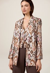 Blazer decorato con paillettes in beige e marrone, caratterizzato da motivi colorati, rever a punta e una vestibilità leggermente accorciata con maniche lunghe.