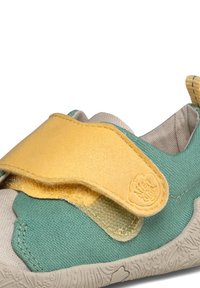 Basket enfant en tissu vert, bride velcro jaune, doublure intérieure beige et semelle blanche texturée, conçue pour une fermeture facile et un confort optimal.