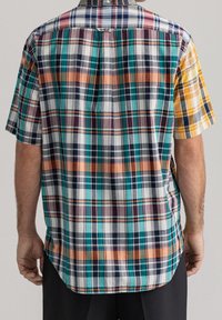 Camisa de cuadros de manga corta con colores vibrantes como verde azulado, naranja, amarillo y azul marino. Fabricada con una tela de patrón a cuadros y un dobladillo redondeado.