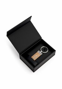Portachiavi in una scatola regalo nera. Anello in metallo argento con un cinturino in pelle marrone chiaro impresso con la scritta "BOSS". La scatola ha una finitura opaca testurizzata.