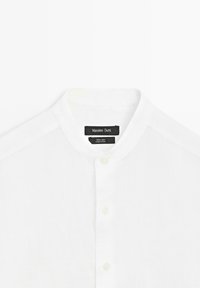 Chemise en lin blanc avec un col officier et des boutons, affichant une étiquette noire avec "Massimo Dutti" et les détails du tissu.