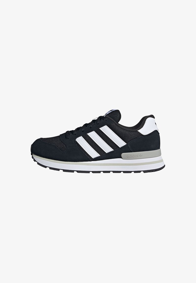 Baskets Adidas noir et blanc avec trois bandes blanches, lacets sur le devant et semelle rembourrée grise sur fond blanc.
