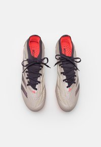 Lichtgrijze sportschoenen met donkerblauwe veters, gestructureerde zijkanten en een felrode binnenkant. Heeft drie diagonale strepen langs de zijkant.