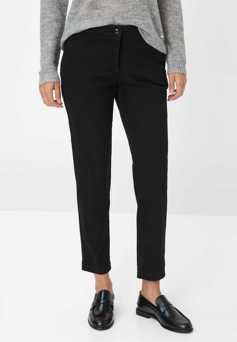 Pantaloni di cotone neri con vestibilità slim, caratterizzati da una chiusura con bottone, tasche standard e orli arrotolati. Indossati con mocassini neri e un maglione grigio.
