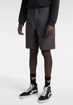 Gray shorts with a straight cut, made of sturdy fabric, featuring a front button closure and side pockets, paired with black sneakers and socks.