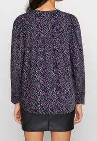 Blusa floreale con maniche lunghe, sfondo viola scuro, piccolo motivo di fiori rosa e verdi, tessuto morbido, scollatura rotonda, dettaglio plissettato sul retro.