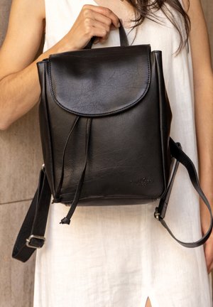 Černý kožený batoh s kulatým klopou, stahovací šňůrkou a nastavitelným popruhem. Disponuje hladkým povrchem a minimálním značením.