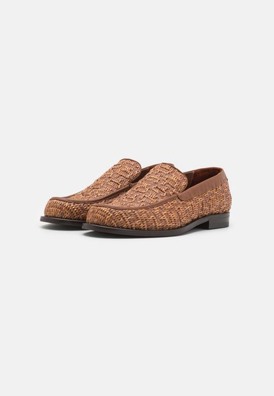 Pruunid kudumistega loafers, millel on sile nahkserv, ümar varvas, tekstureeritud ülemine osa ja lame tall. Disainitud libisemisega stiilis.