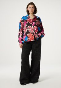 Bloemmotief blouse in zwart, roze, blauw en rood, gecombineerd met wijdvallende zwarte geweven broek. Blouse heeft een kraag en knopen.