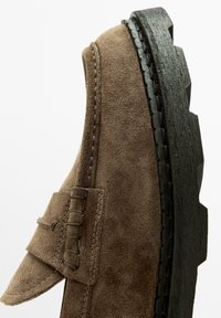 Brauner Wildlederschuh mit abgerundetem Zehenbereich, einer seitlichen Naht und einer dicken schwarzen Gummisohle mit strukturierter Oberfläche und erhöhter Profilsohle.